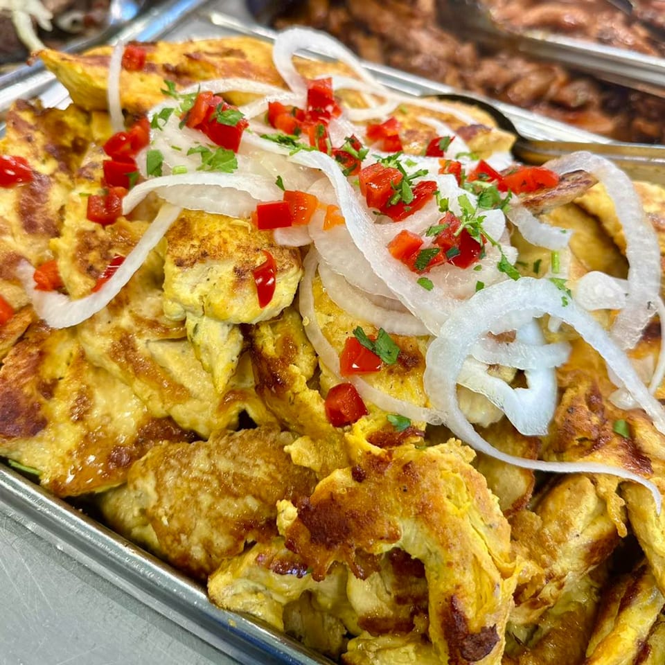 A tray of golden-brown Cuban tortillas topped with sliced onions, diced red peppers, and fresh herbs.