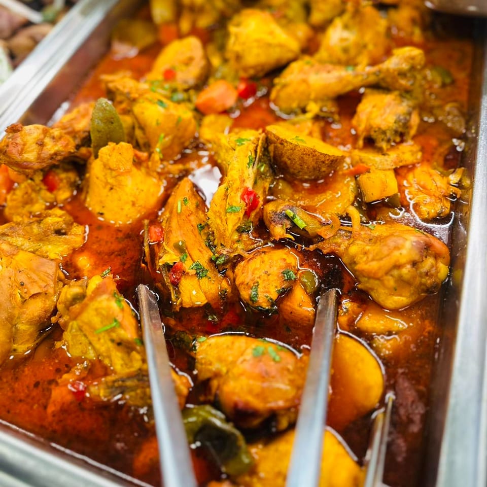 Close-up of Cuban chicken fricassee with vegetables in a rich red sauce, served in a metal tray.