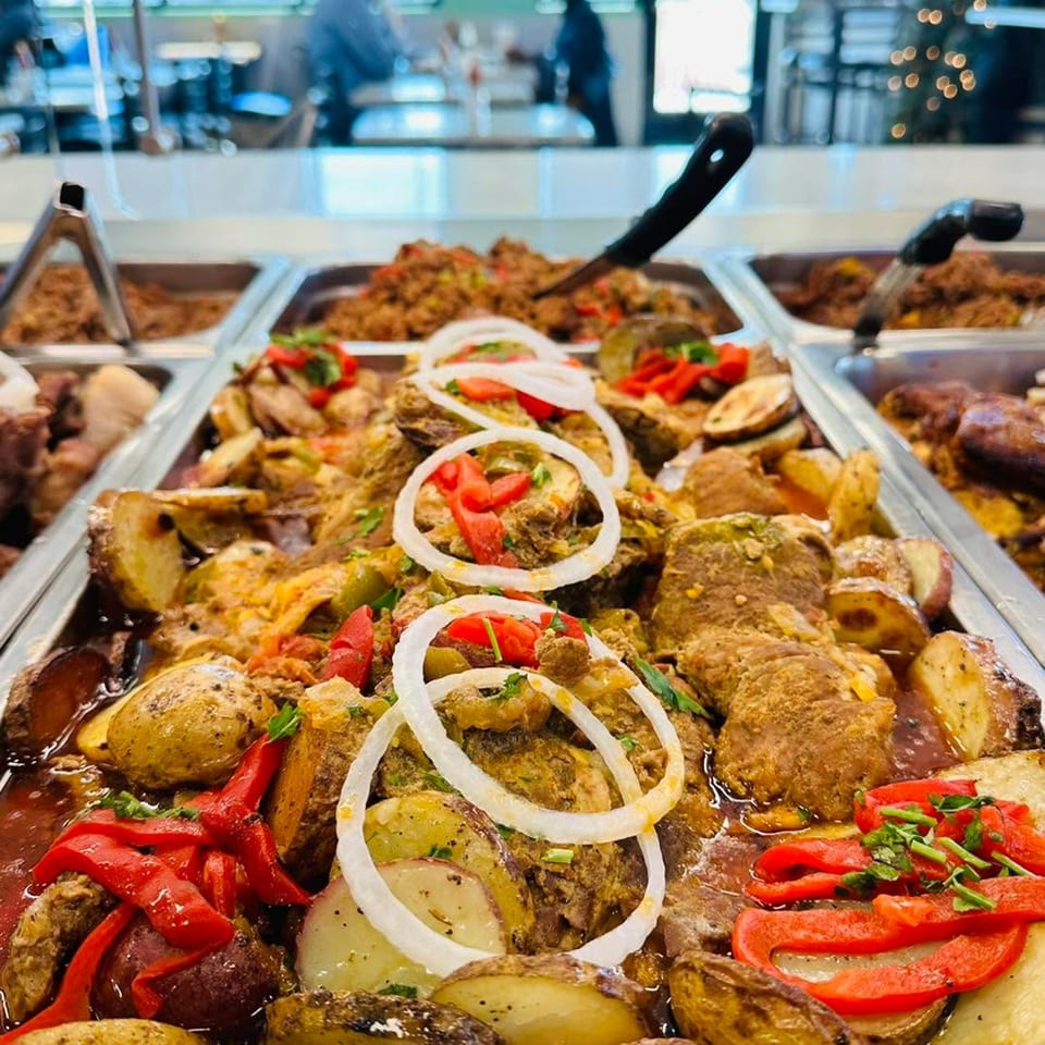 Cuban-style roasted pork with potatoes, red peppers, and onions in a buffet tray.
