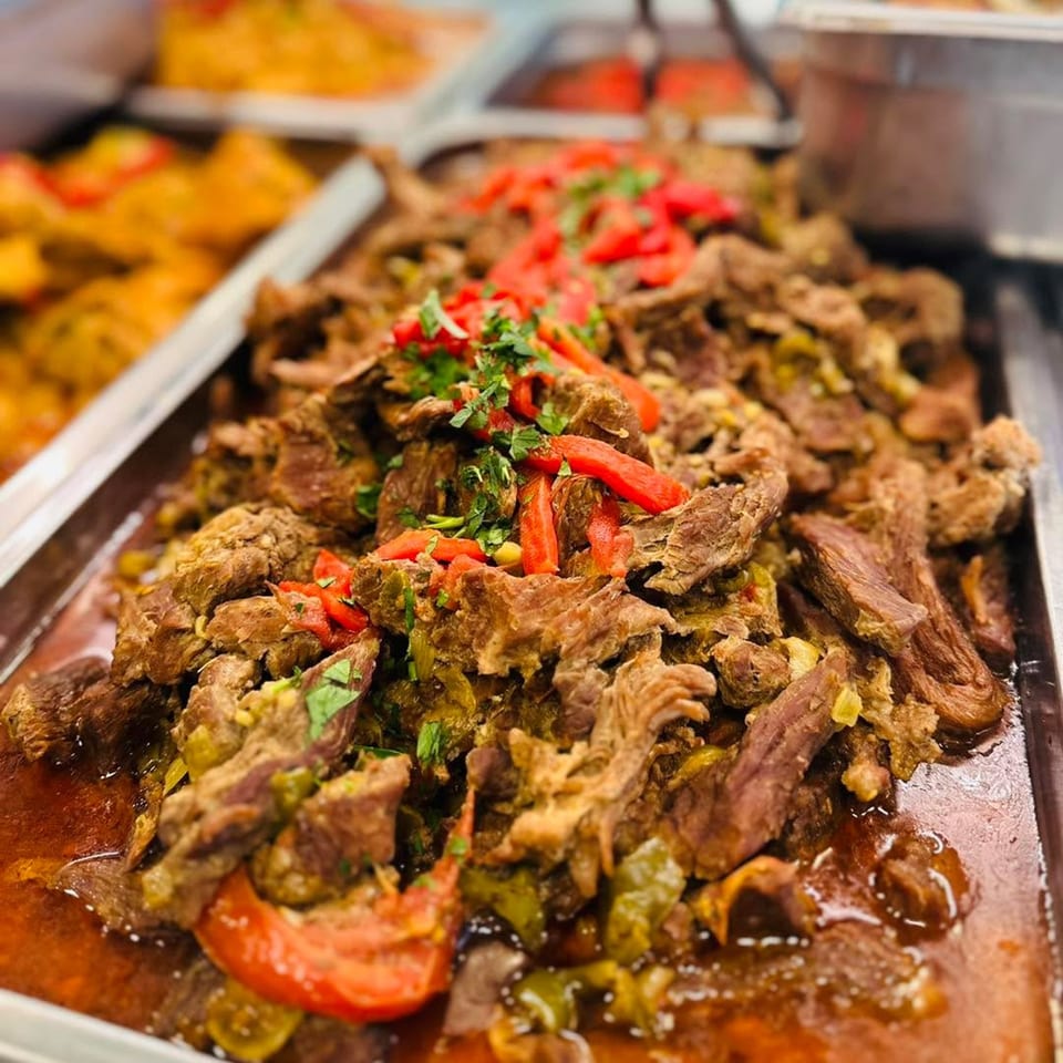 Close-up of Cuban shredded beef (Ropa Vieja) with red peppers and cilantro in a serving tray.