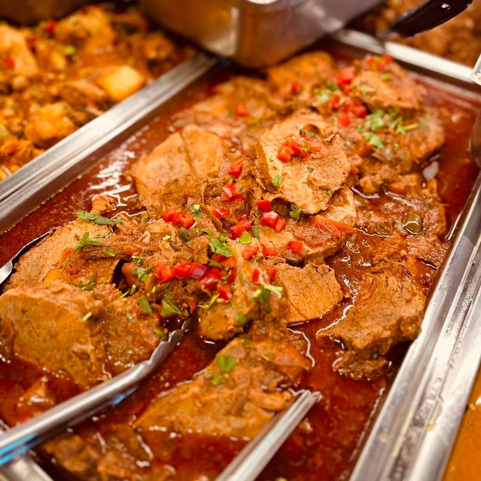 Close-up of Cuban shredded beef (Ropa Vieja) with red peppers and cilantro in a serving tray.