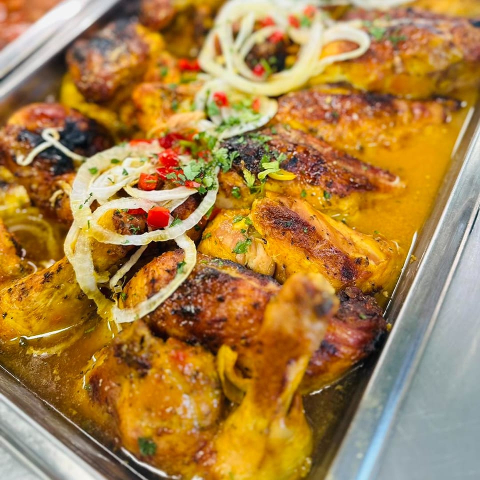 Close-up of Cuban roasted chicken pieces in a savory sauce, topped with sliced onions and peppers.