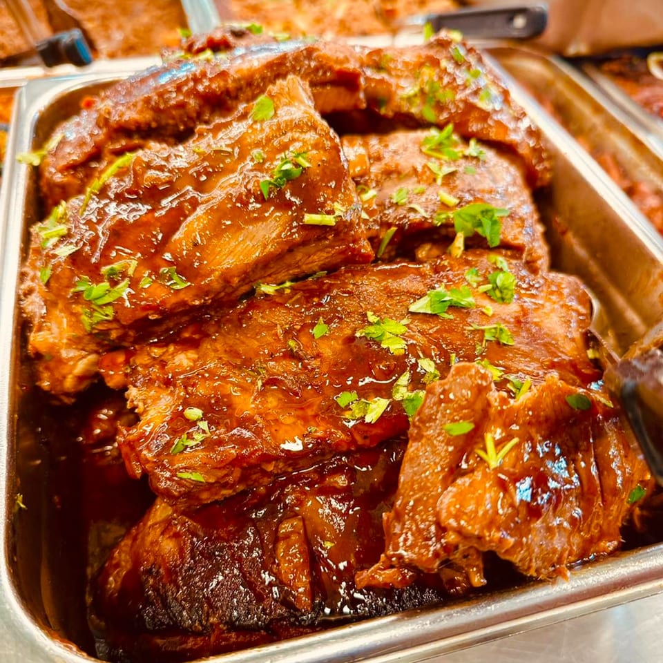 Close-up of saucy Cuban ribs with fresh parsley in a metal serving tray.